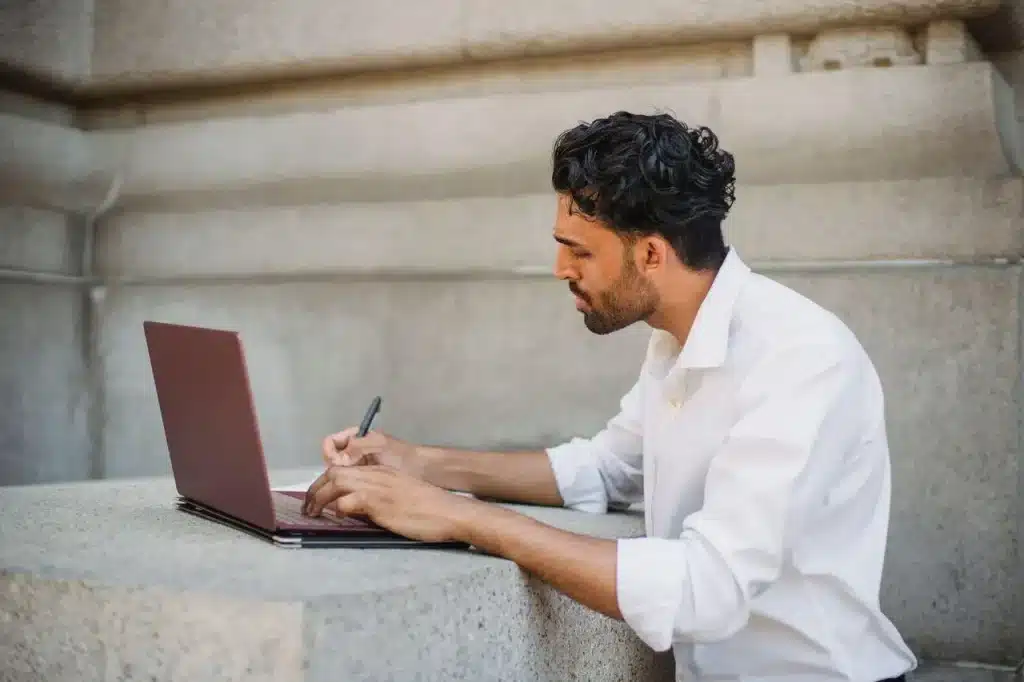 Man in white shirt working on laptop outdoors at stone table