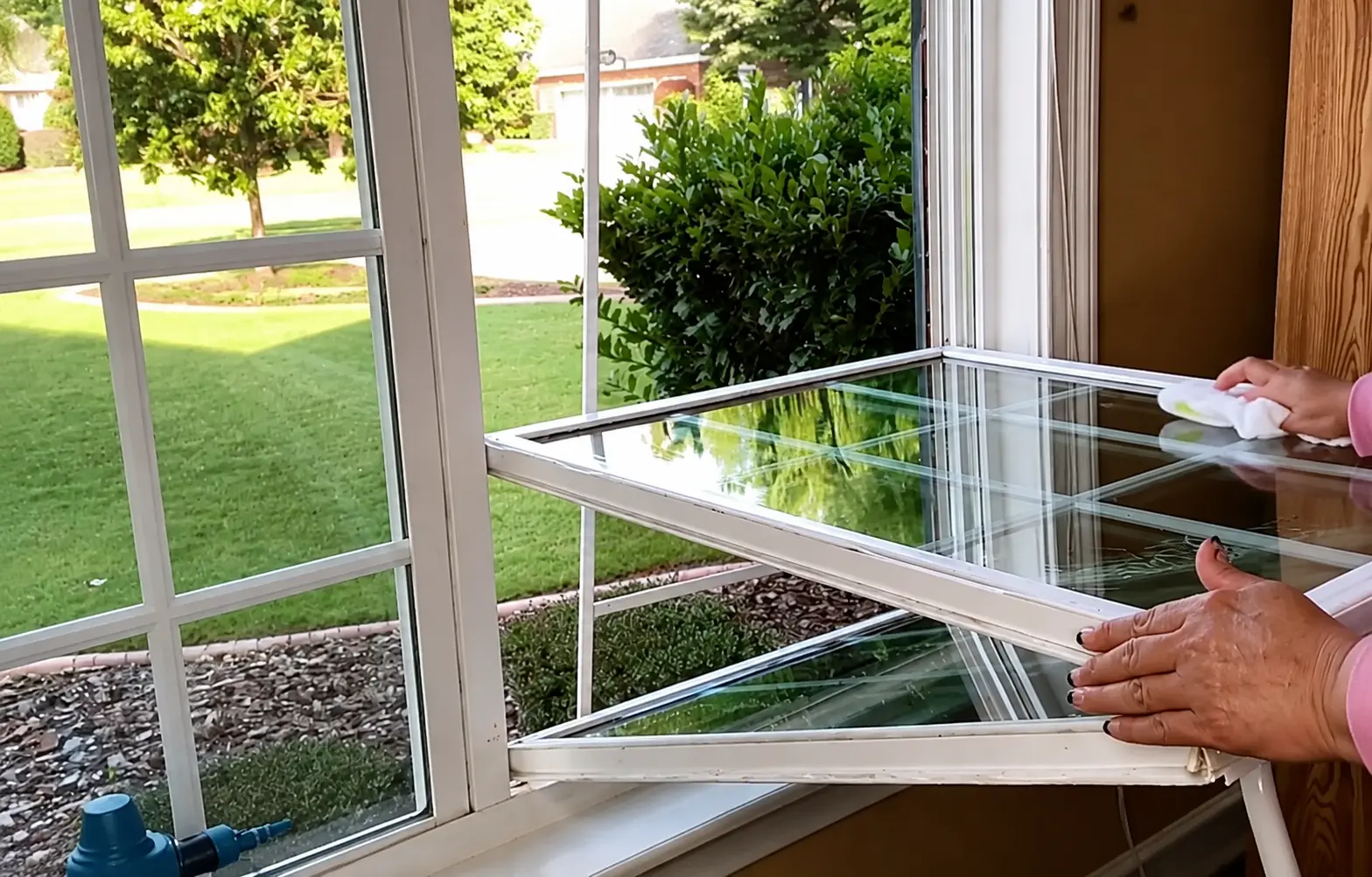 person cleaning a glass window panel with a cloth while holding the white window frame open
