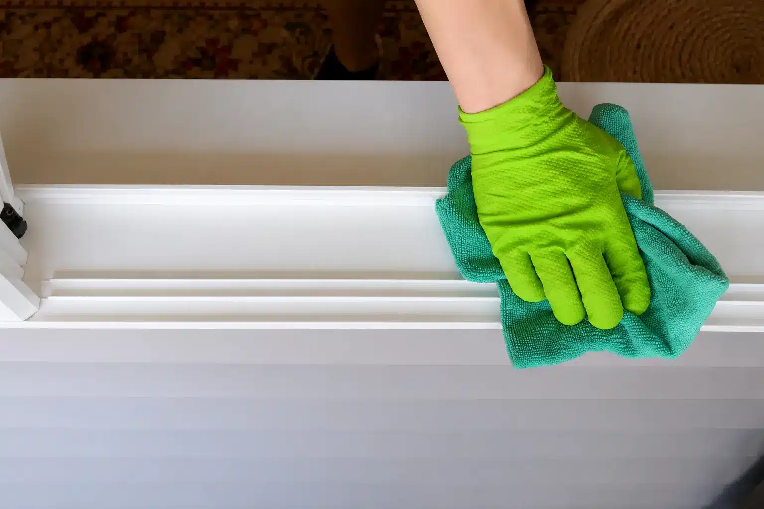 gloved hand wiping a clean white window track with a green microfiber cloth