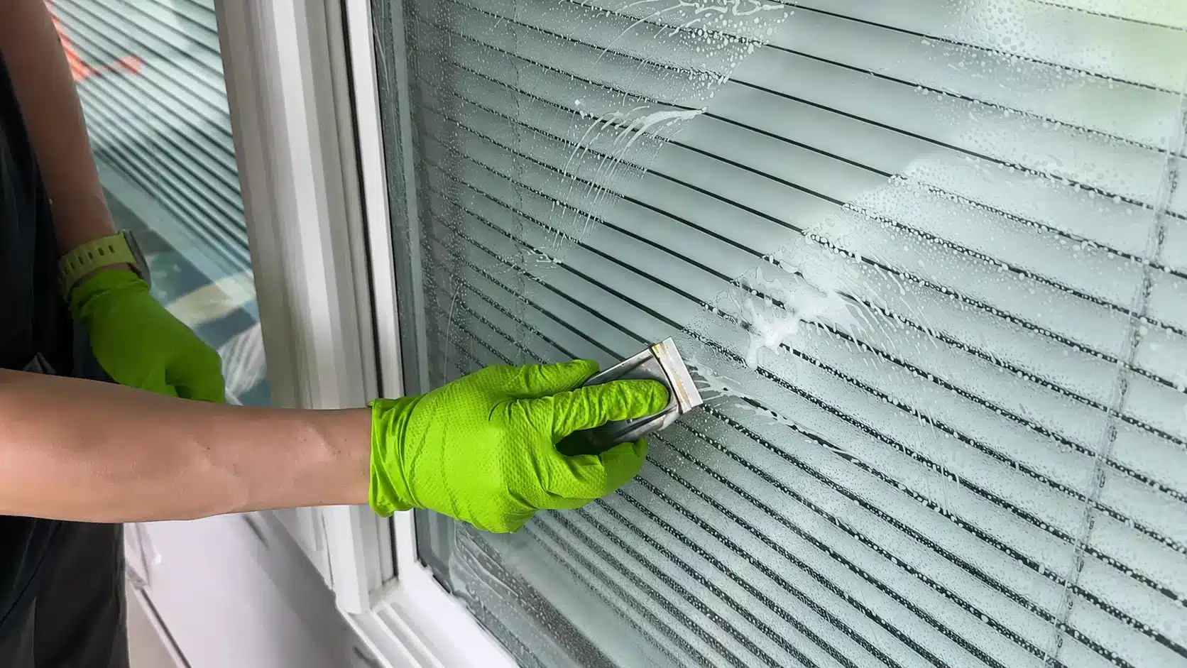 person in green gloves cleaning a soapy window with a handheld squeeg