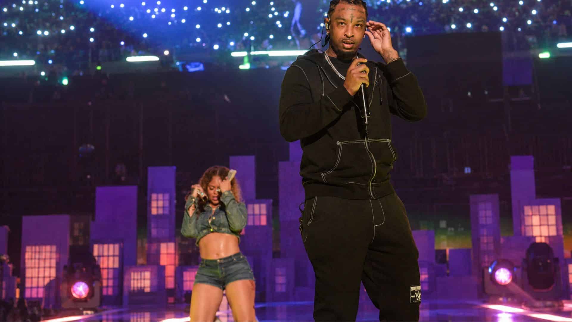 21 Savage performing on stage in a black outfit with a microphone during a live concert.