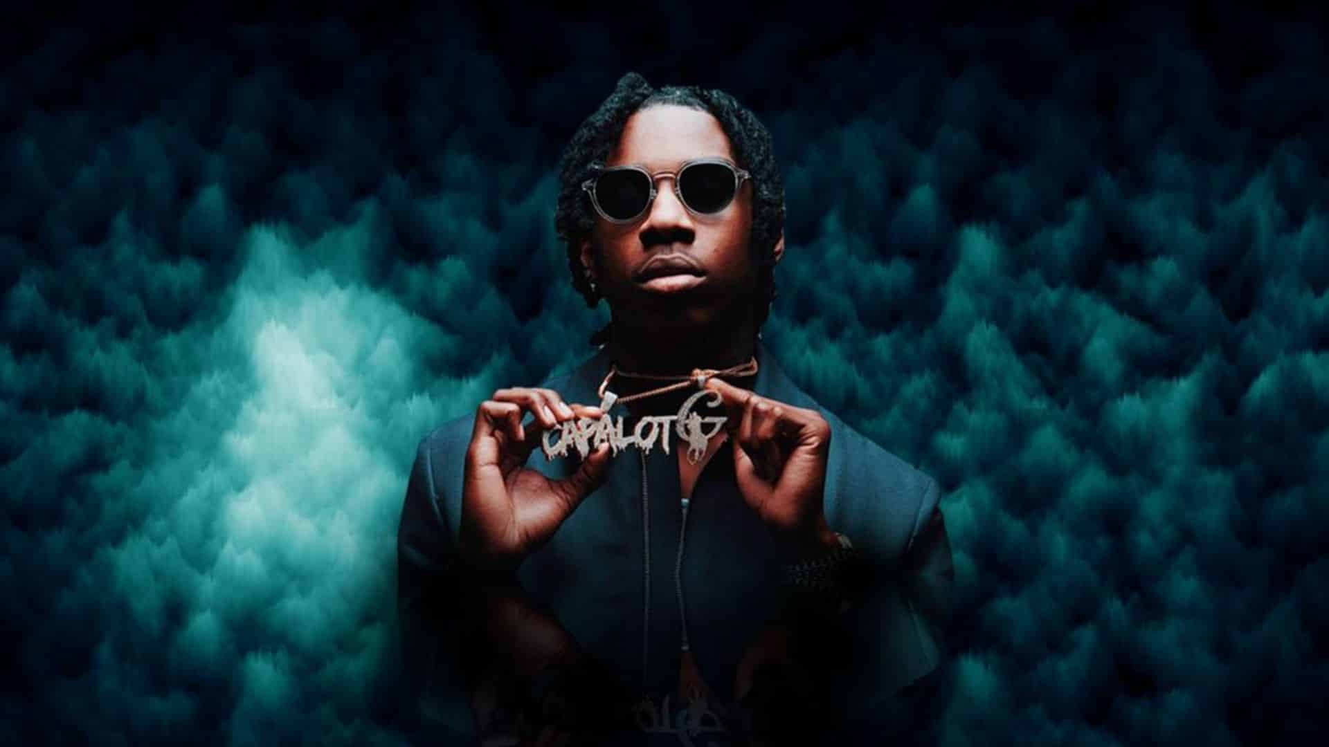 American rapper Polo G wearing sunglasses and a dark outfit while holding a chain against a blue-toned background.