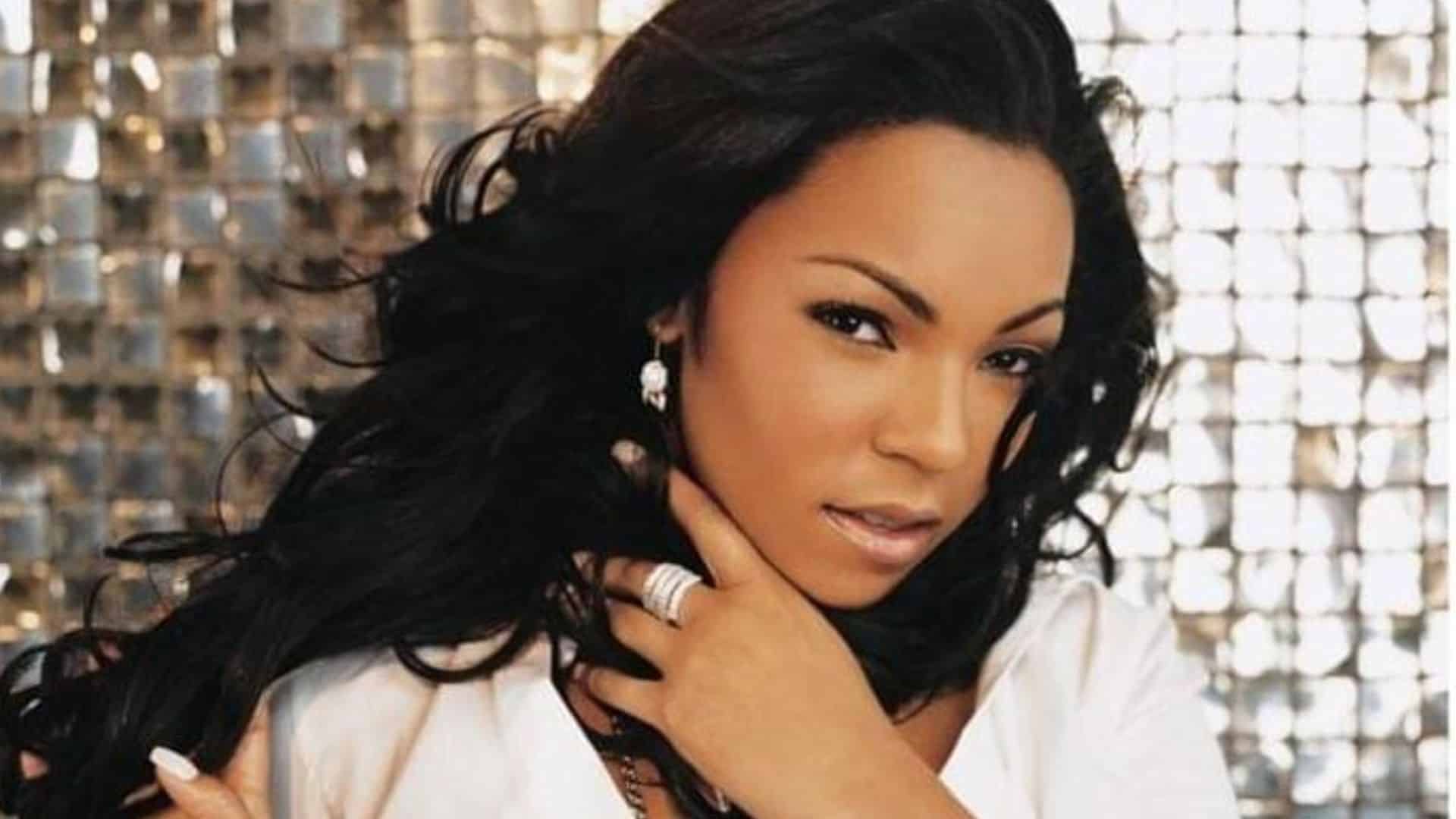 Ashanti posing for a portrait with long dark hair wearing a white top against a patterned background