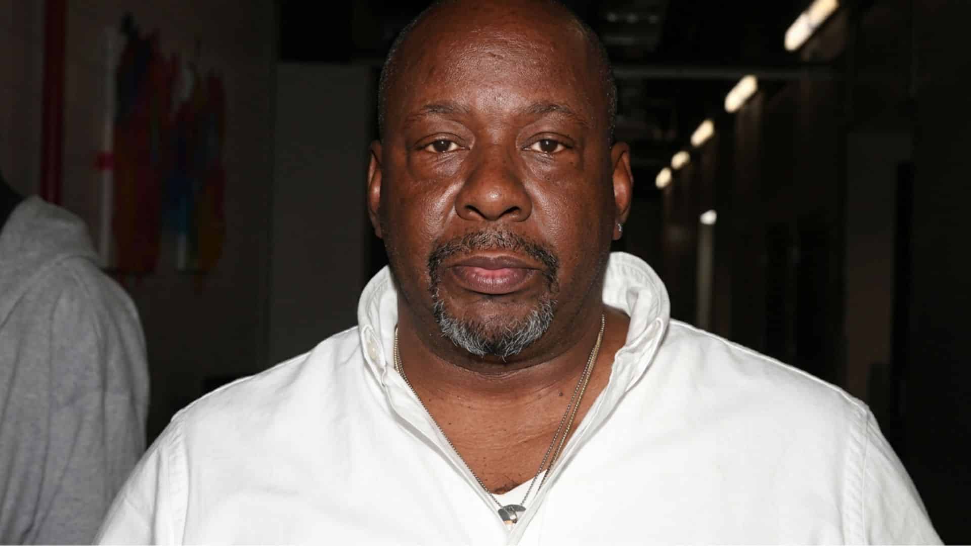 Bobby Brown posing for a portrait wearing a white shirt with a serious expression in an indoor setting