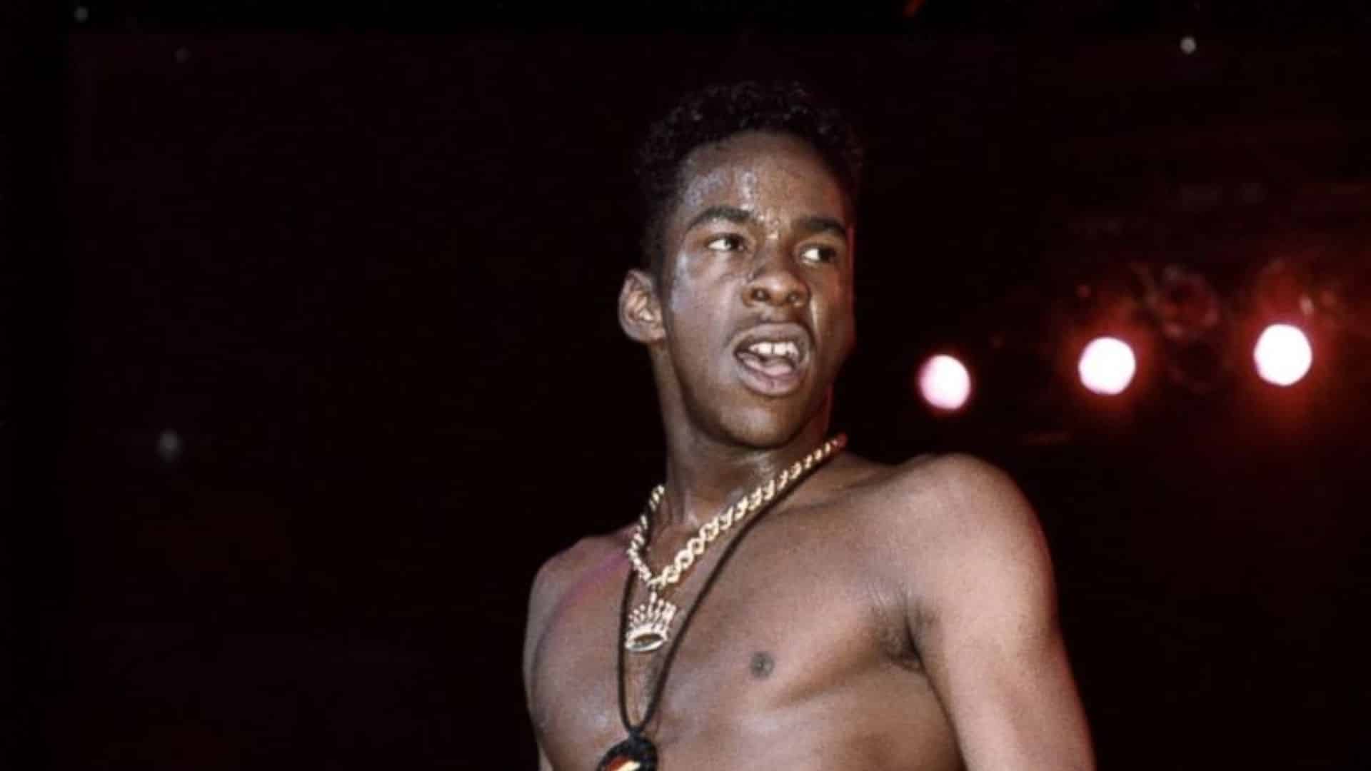 Bobby Brown performing on stage shirtless with a necklace under dramatic lighting during an early music career appearance