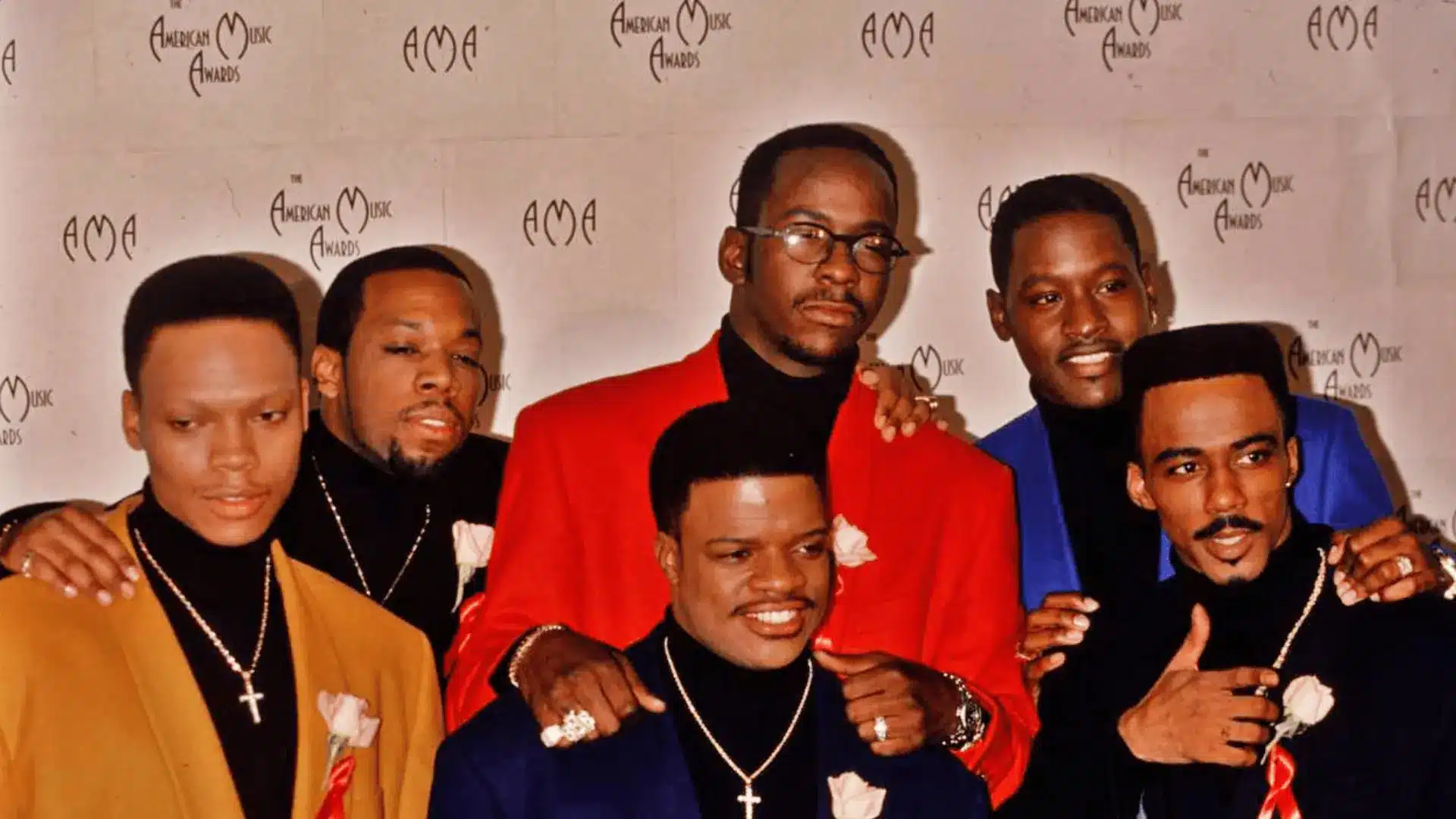 Bobby Brown standing with New Edition members at an American Music Awards event wearing colorful formal outfits
