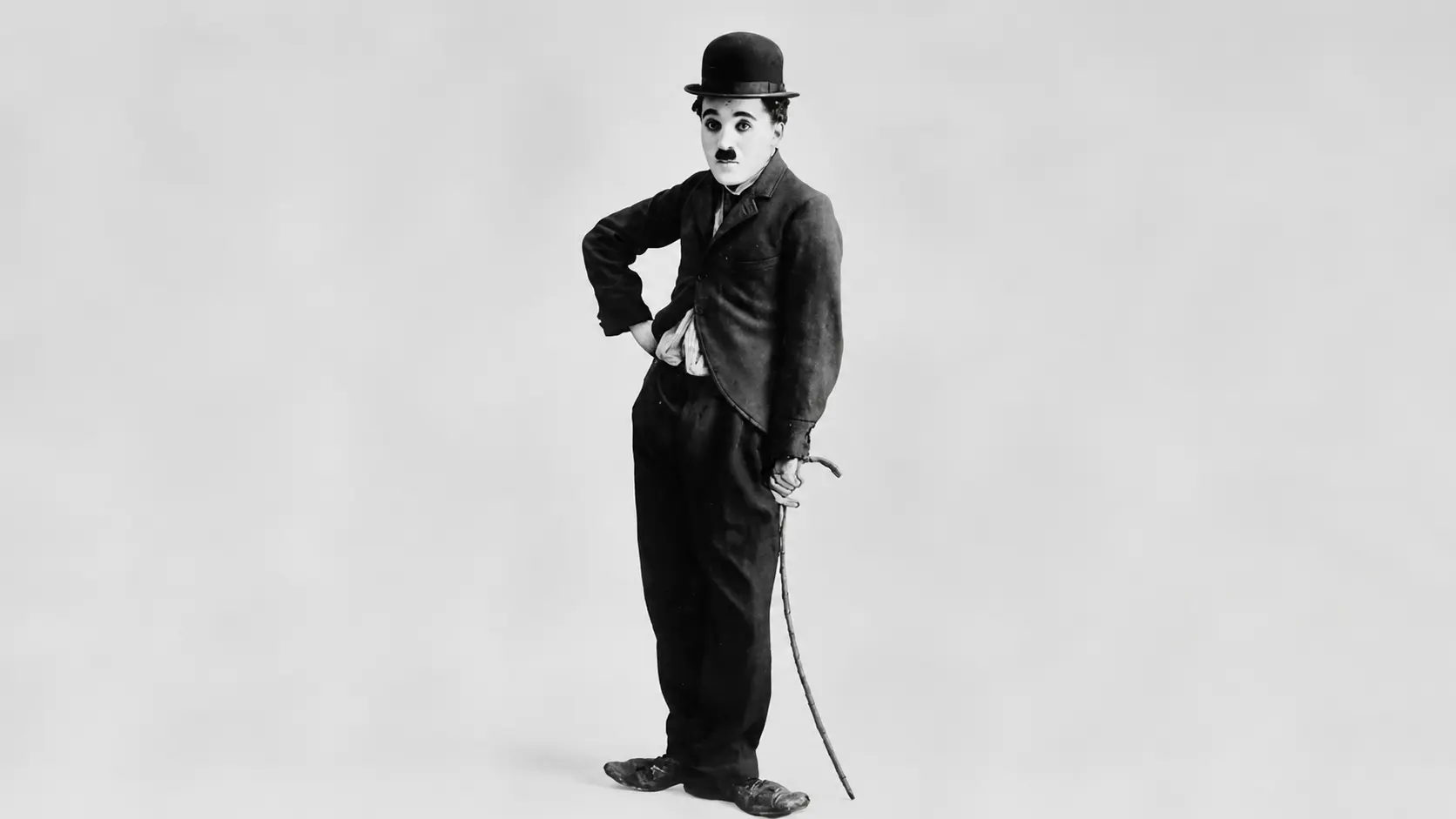 Charlie Chaplin wearing a bowler hat and suit holding a cane in a classic studio pose