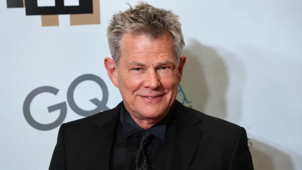 Portrait of David Foster in a black suit with gray hair smiling at an event backdrop with professional lighting and style