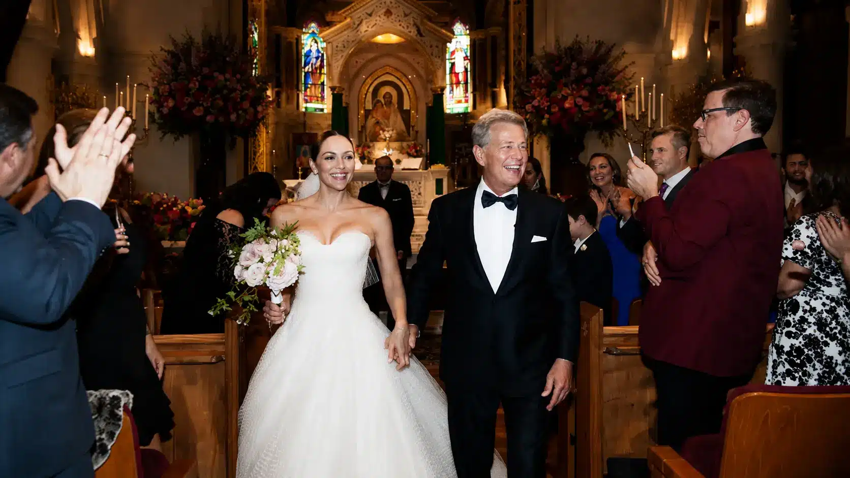Wedding ceremony inside a cathedral showing david foster and Katharine McPhee walking down aisle with guests applauding warmly