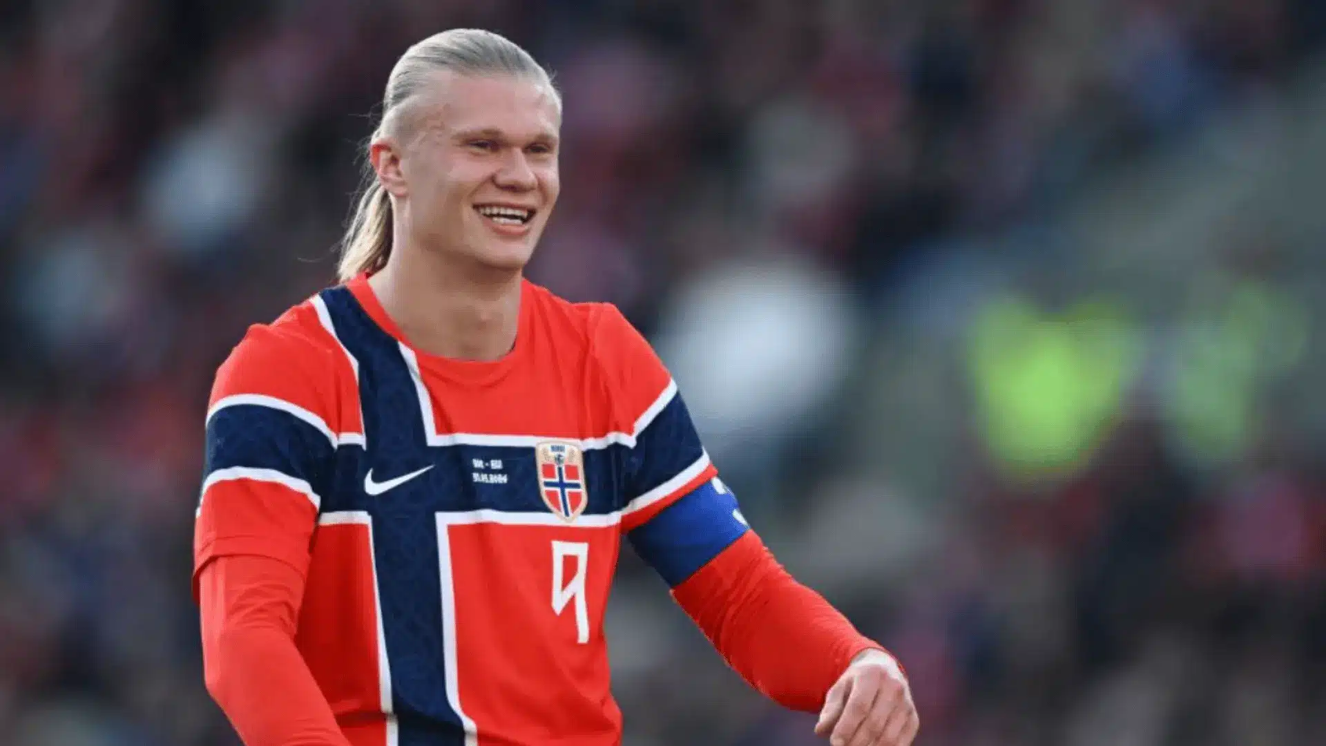 Erling Haaland smiles while wearing Norway’s number nine soccer jersey and captain’s armband.