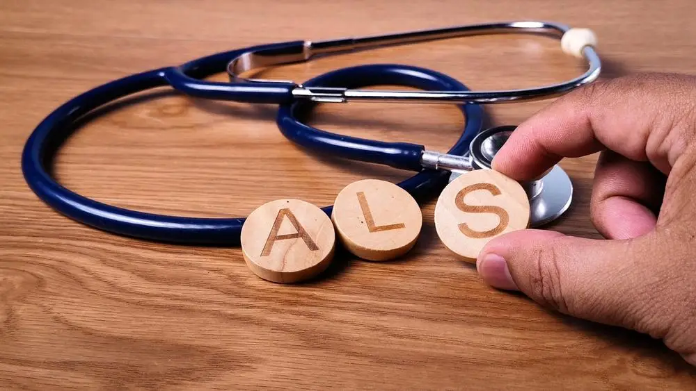 Stethoscope on wooden surface with hand holding wooden discs spelling ALS