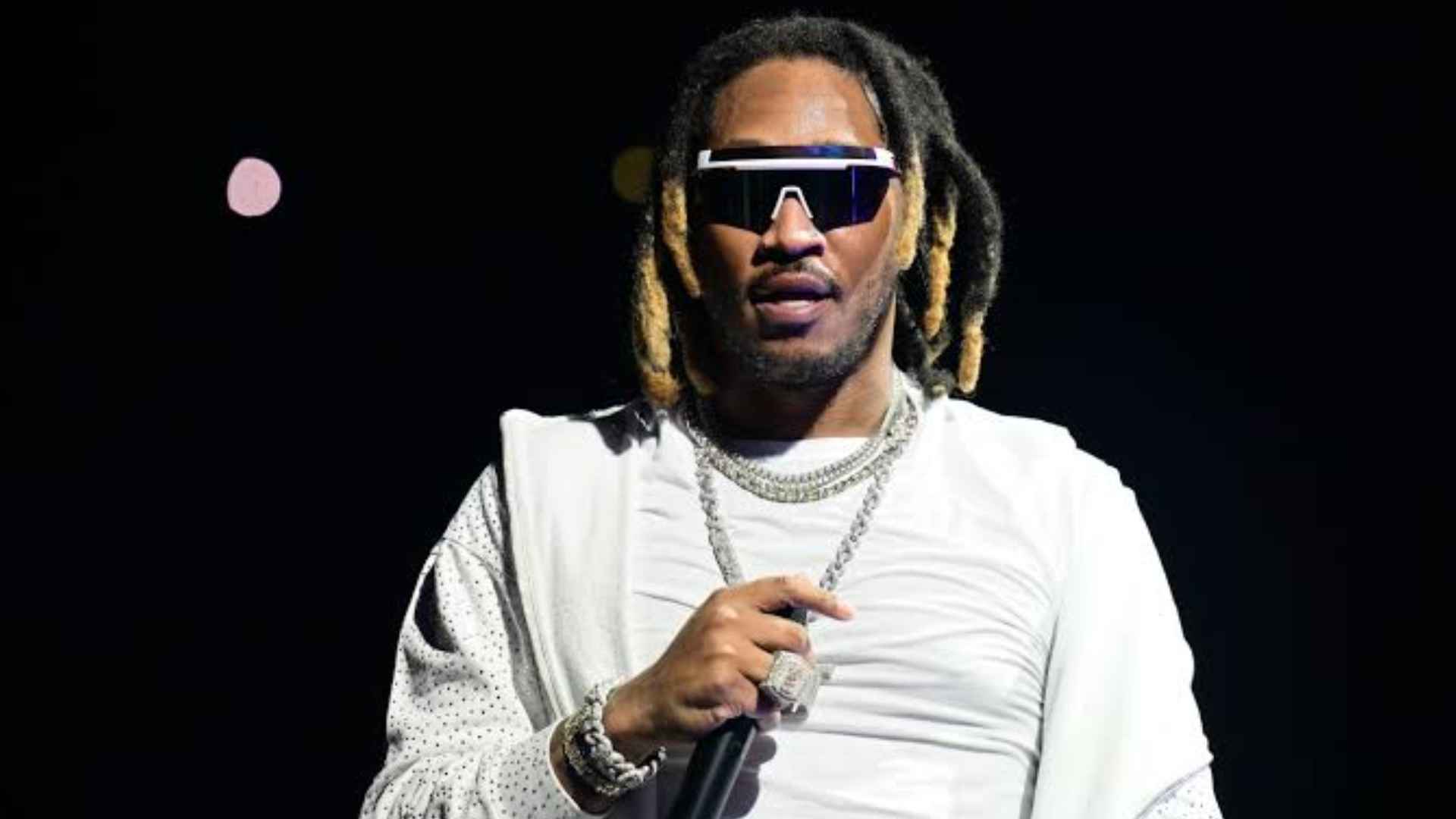 Future performing on stage wearing sunglasses and a white outfit while holding a microphone during a concert.