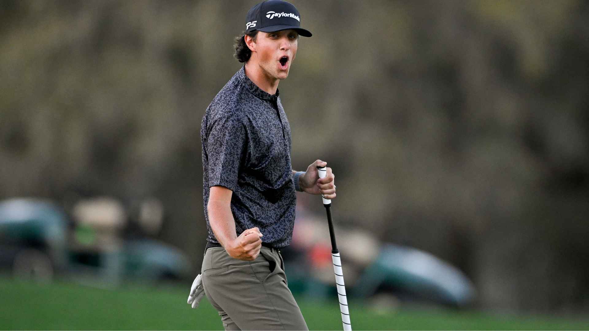 Grant Horvat wearing TaylorMade cap and patterned shirt celebrates on the course while holding a club during a competitive moment