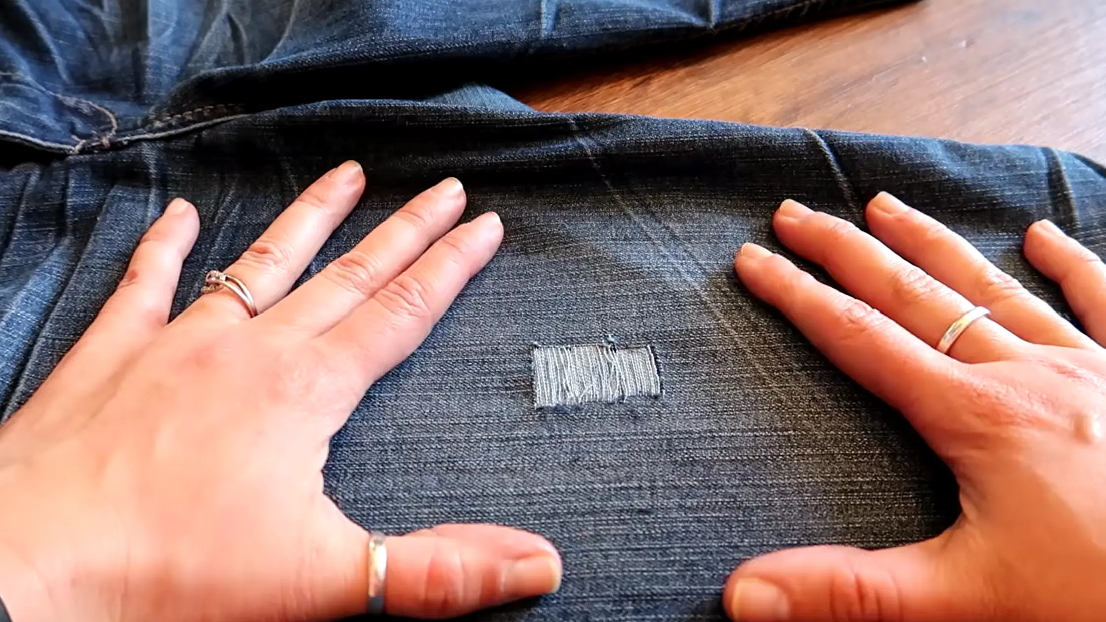 Hands adjusting the shape of a distressed jeans cut with frayed white threads showing