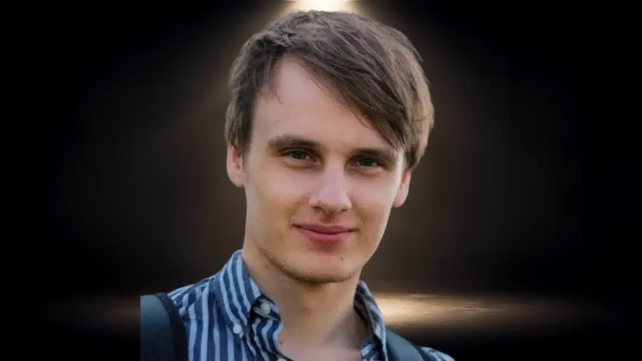 Headshot of Fabian Hedin smiling in a blue-striped collared shirt against a dark background.