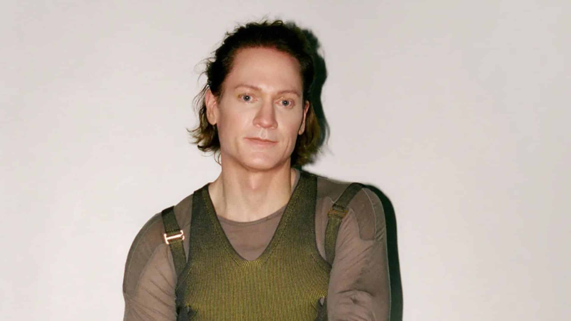Bryan Johnson standing indoors wearing a dark vest while discussing his investment choices and wealth management strategies
