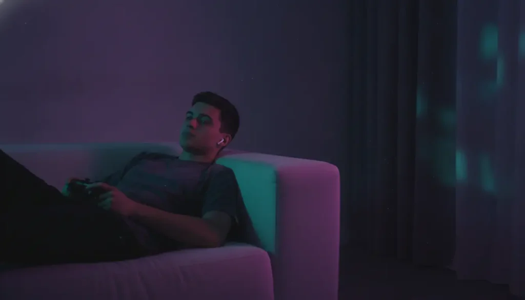Young man relaxing on a sofa playing video games in a dimly lit room