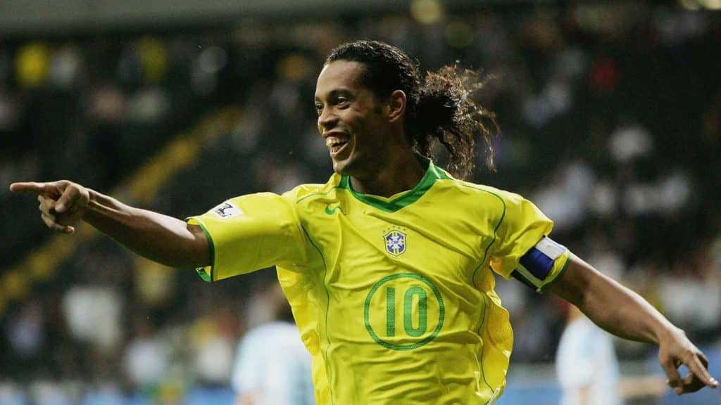 Ronaldino in yellow national team jersey celebrating during a match with arms stretched and a smile on the field