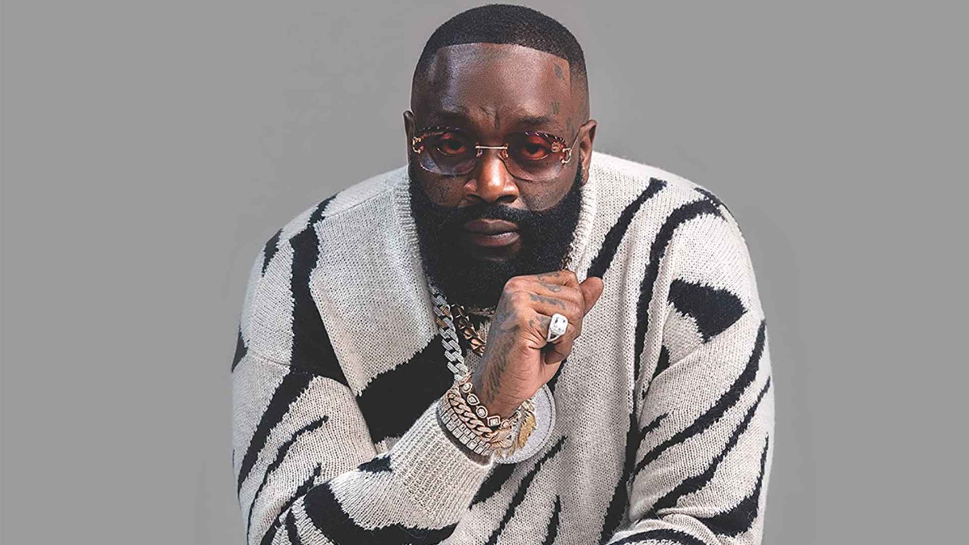 Rick Ross wearing sunglasses and a black and white sweater during a portrait photoshoot.