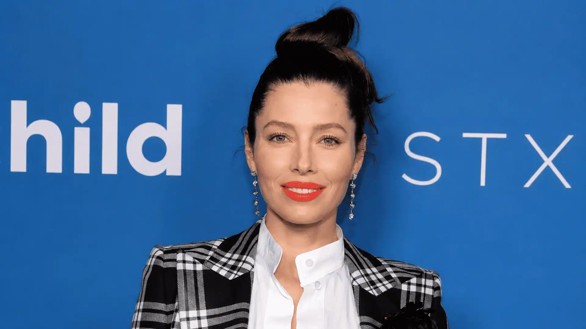 Jessica Biel wearing a black and white plaid blazer with her dark hair in a high bun at a blue carpet event