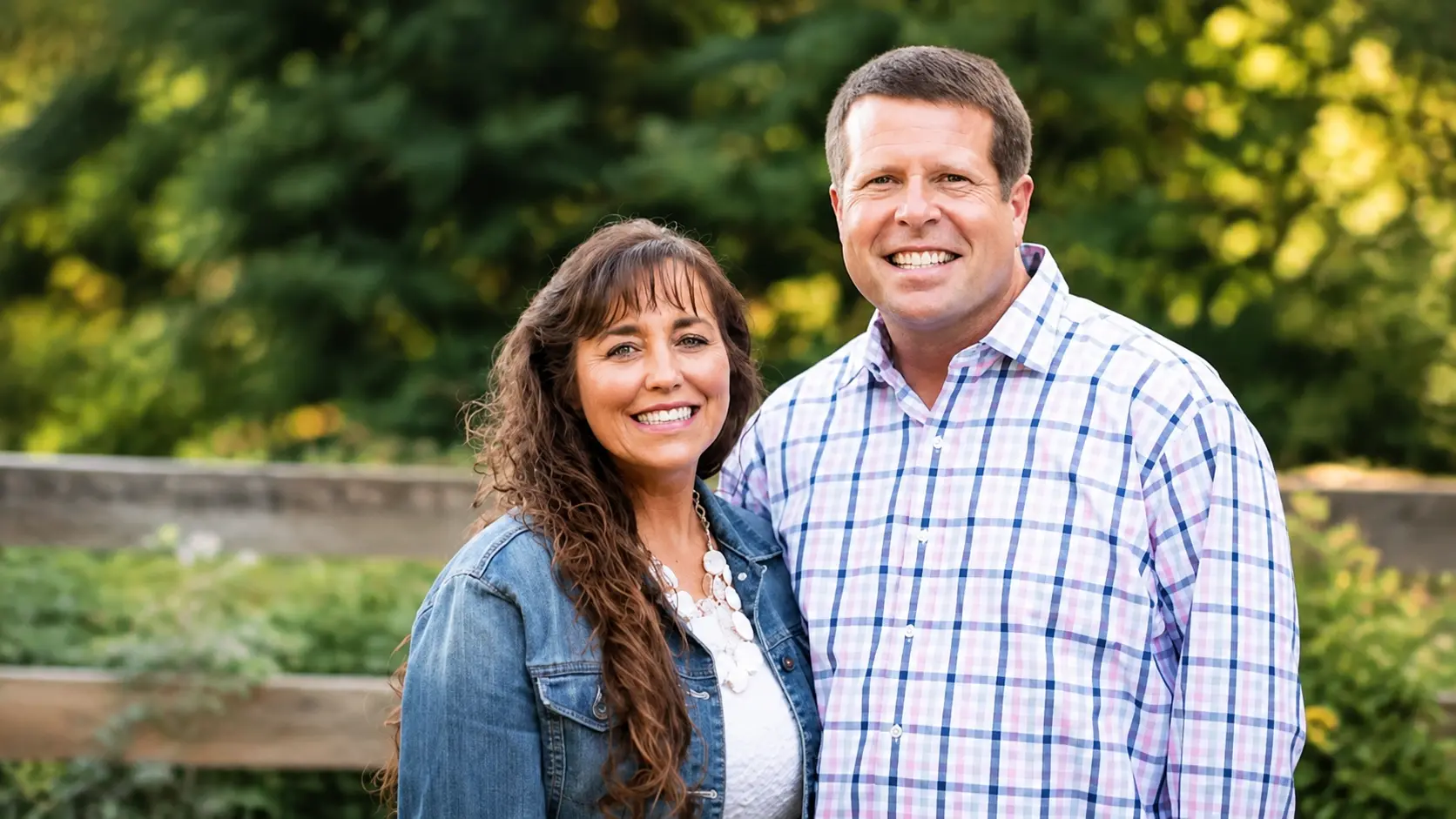 Jim Bob & Michelle Duggar posing together outside with trees behind them and relaxed expressions in a bright outdoor portrait