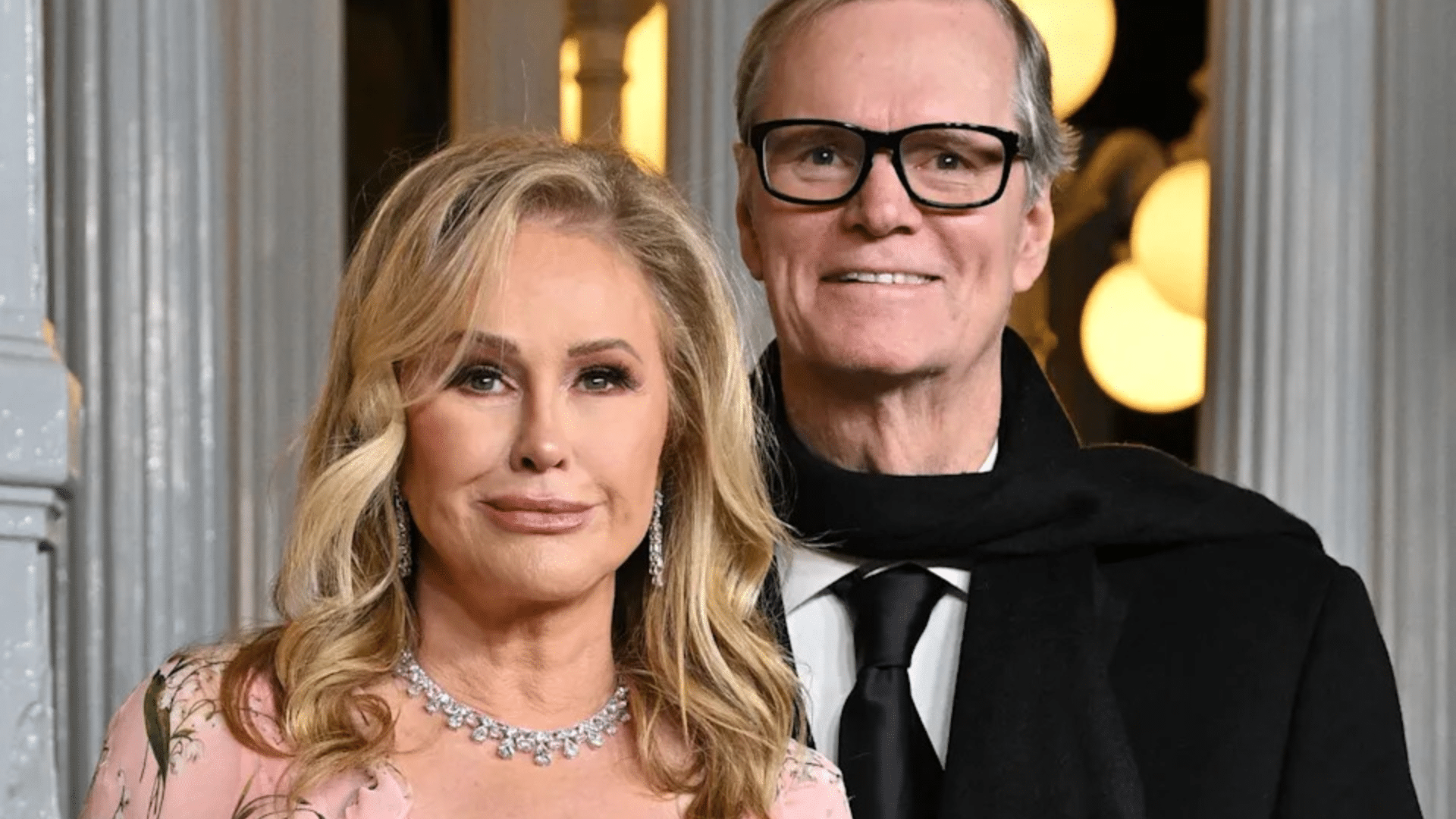 Kathy Hilton and Rick Hilton posing together at an event with formal outfits and an indoor backdrop behind them