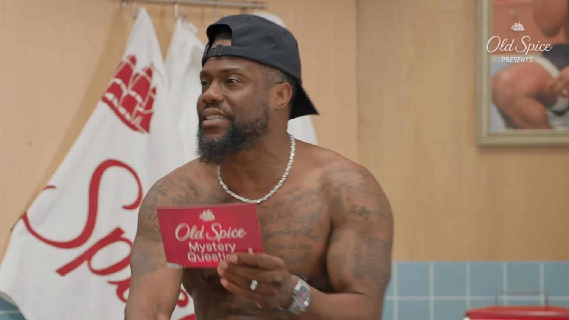 Kevin Hart holding an Old Spice card during a brand campaign scene with product branding visible in the background