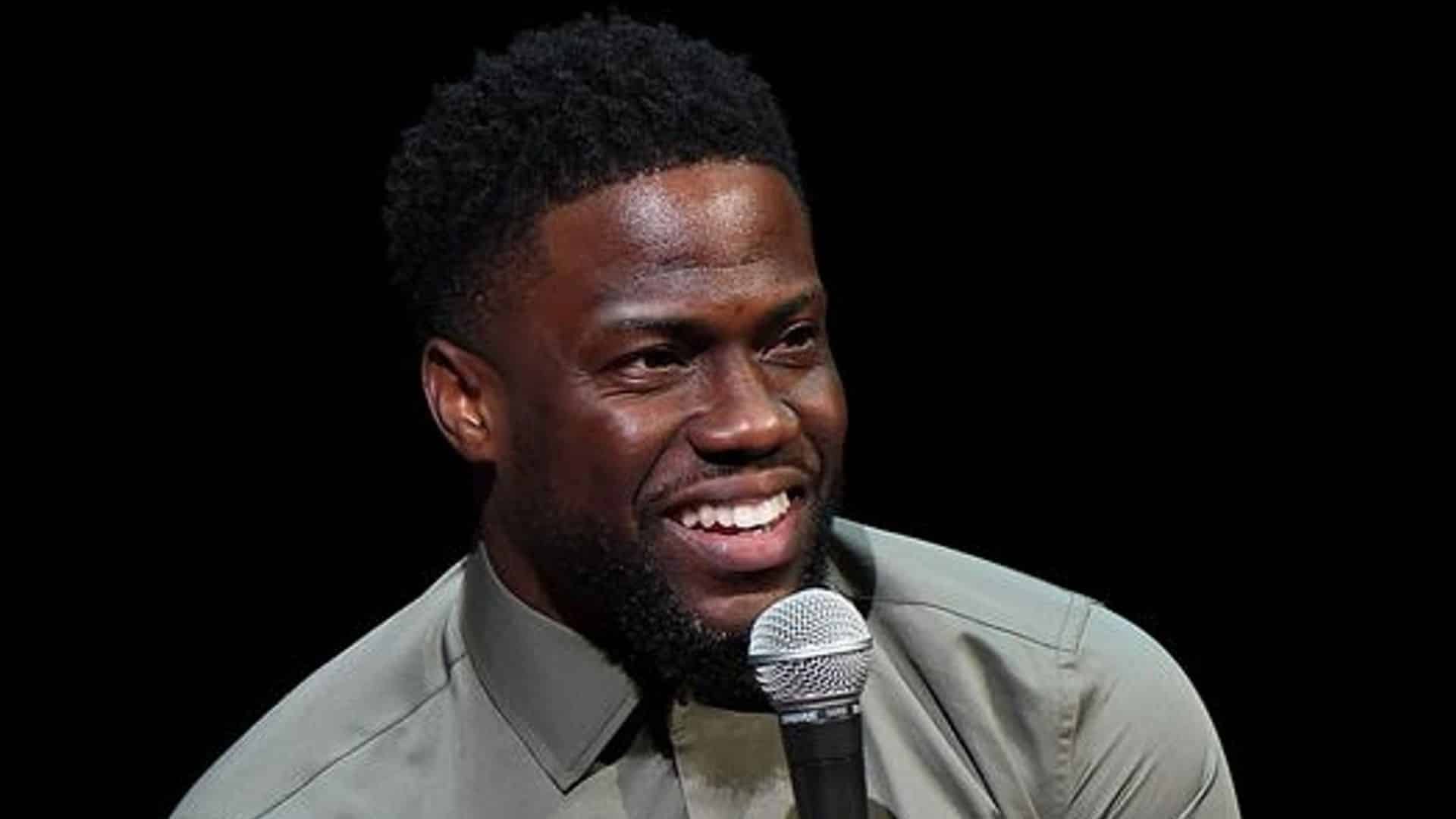 Kevin Hart speaking into a microphone during an early comedy performance with a dark background and casual outfit