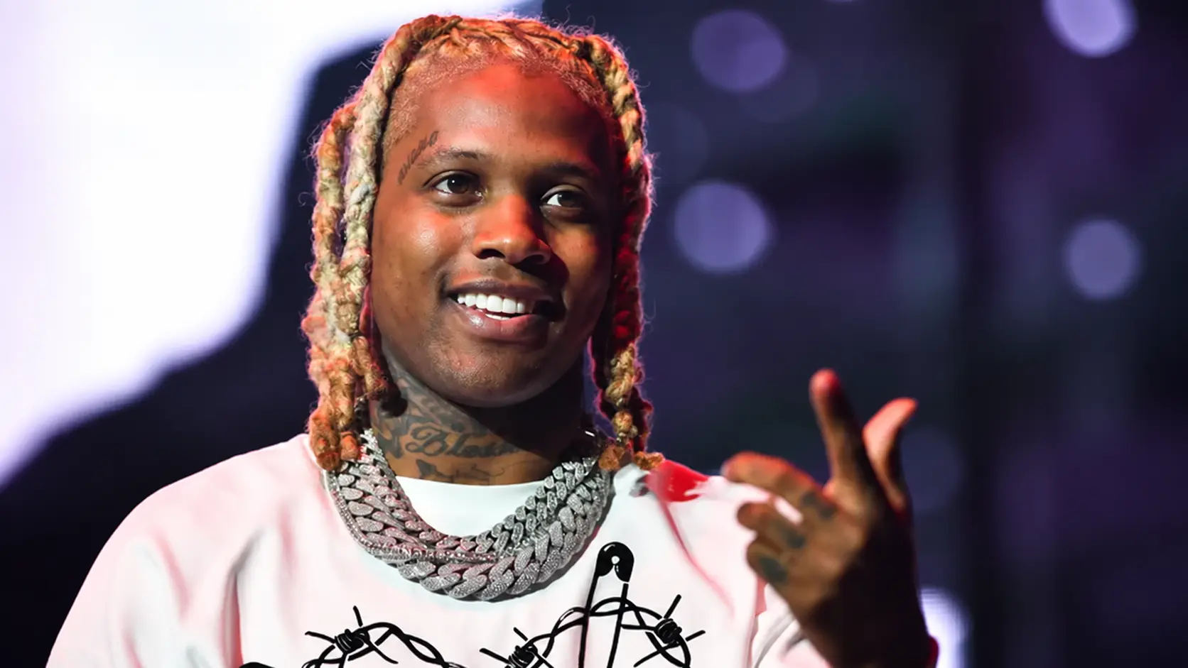 Lil durk performing on stage with blond dreadlocks diamond chains and pink outfit under colorful concert lights night