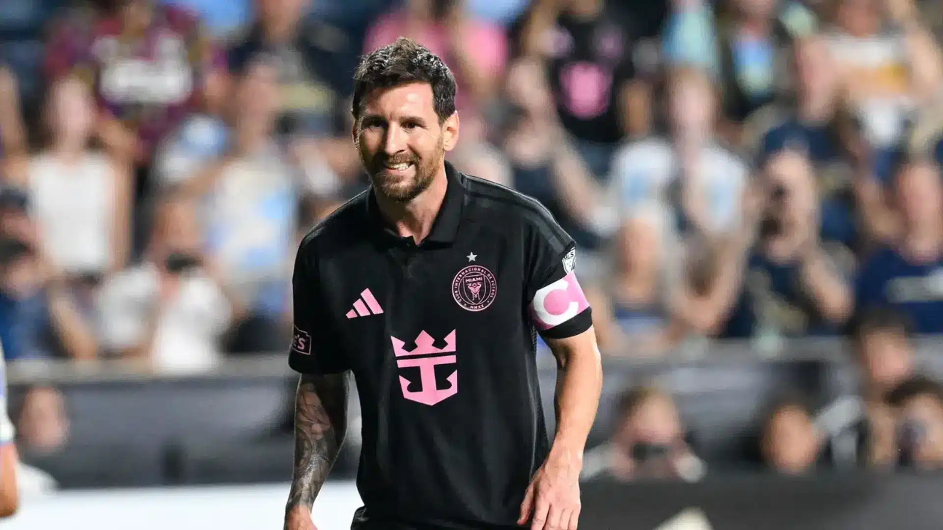 Lionel Messi smiling on the field in a black Inter Miami jersey with pink accents and a captain's armband.