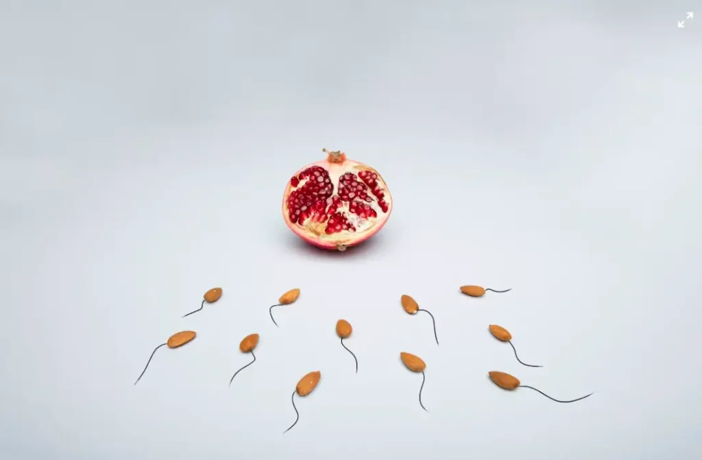 Halved pomegranate with almond-shaped objects on light background
