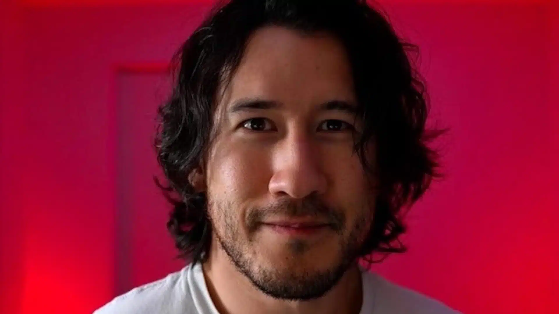 Male gaming creator smiling at the camera against a vivid red and pink studio background