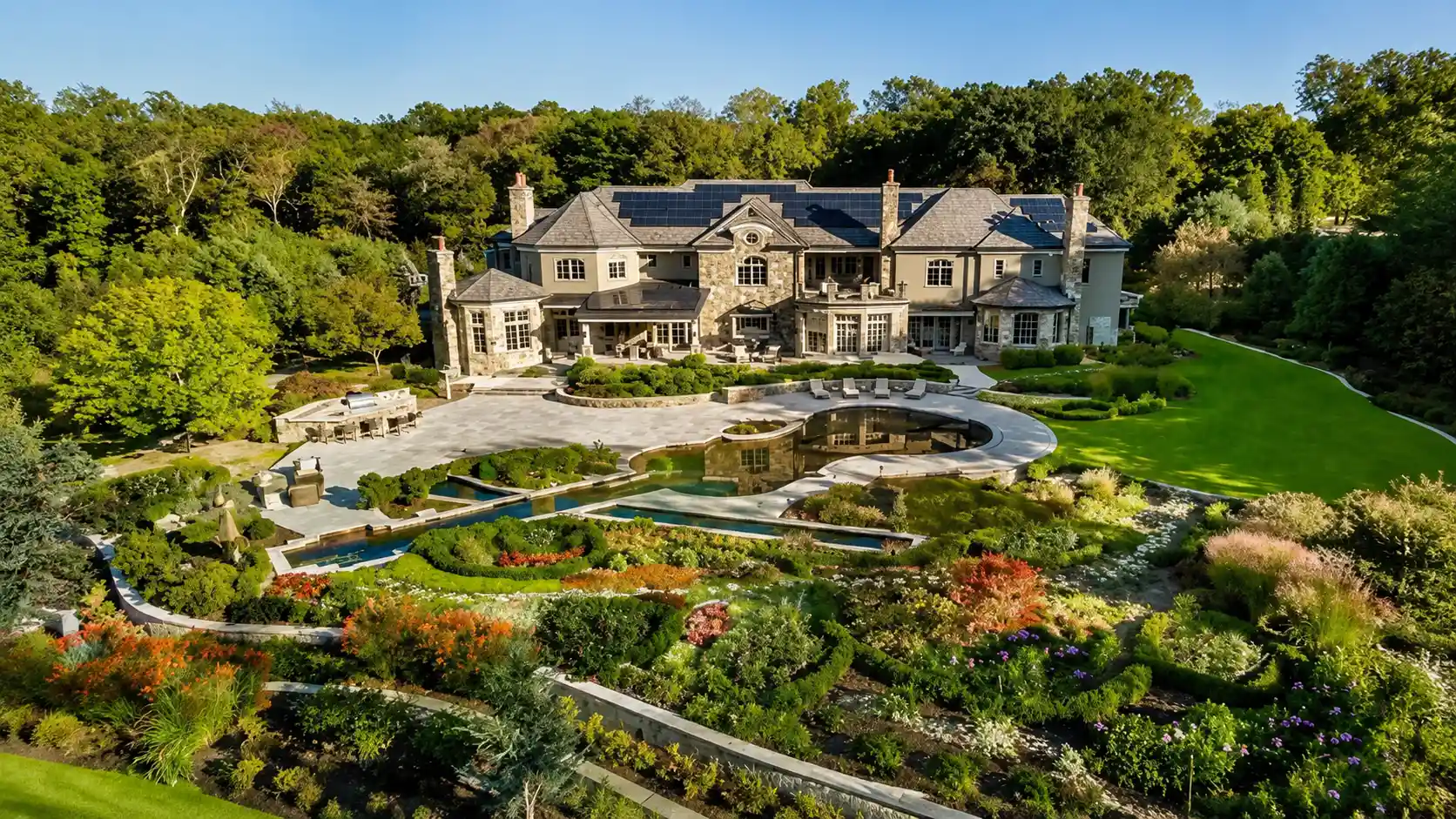Mariah Carey's Westchester estate surrounded by lush gardens trees and water features with landscaped grounds under clear blue sky