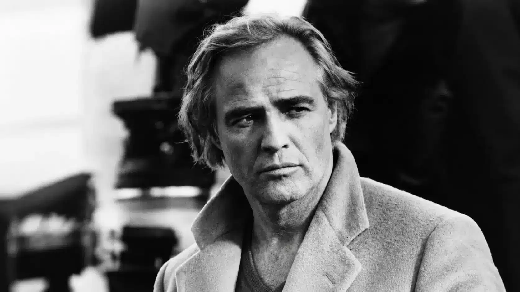 Marlon Brando wearing a coat with a serious expression in a classic vintage style setting