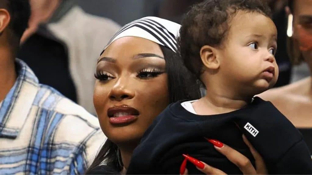 Megan Thee Stallion holding a young child at a public event as the child looks to the side.