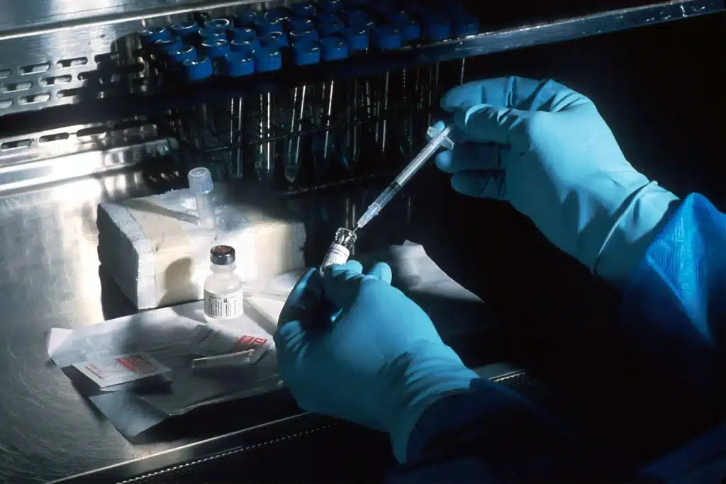 Gloved hands preparing a syringe in a laboratory with test tubes in background