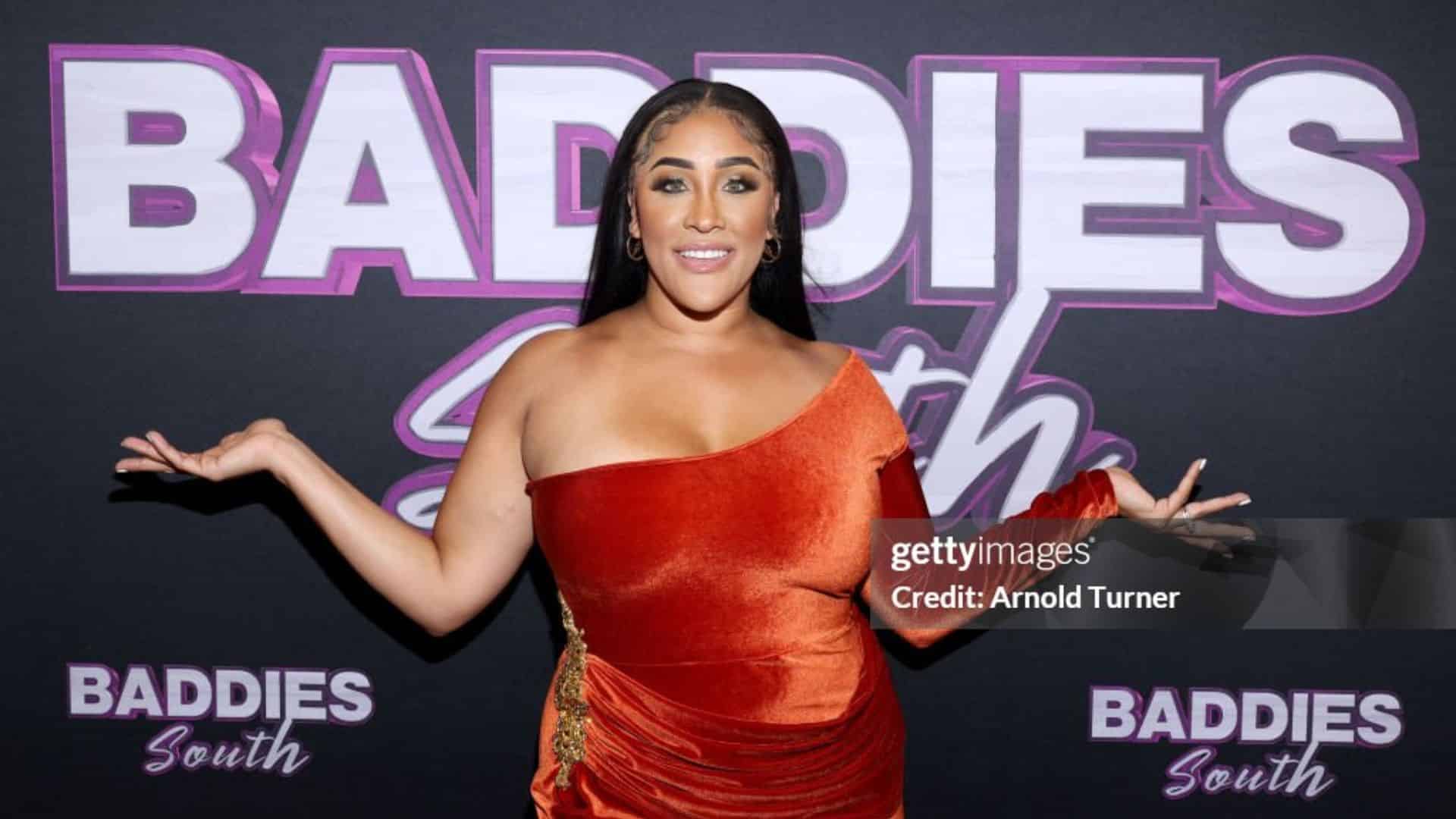 Natalie Nunn posing at a public appearance for baddies wearing a black dress with statement jewelry and sleek hairstyle