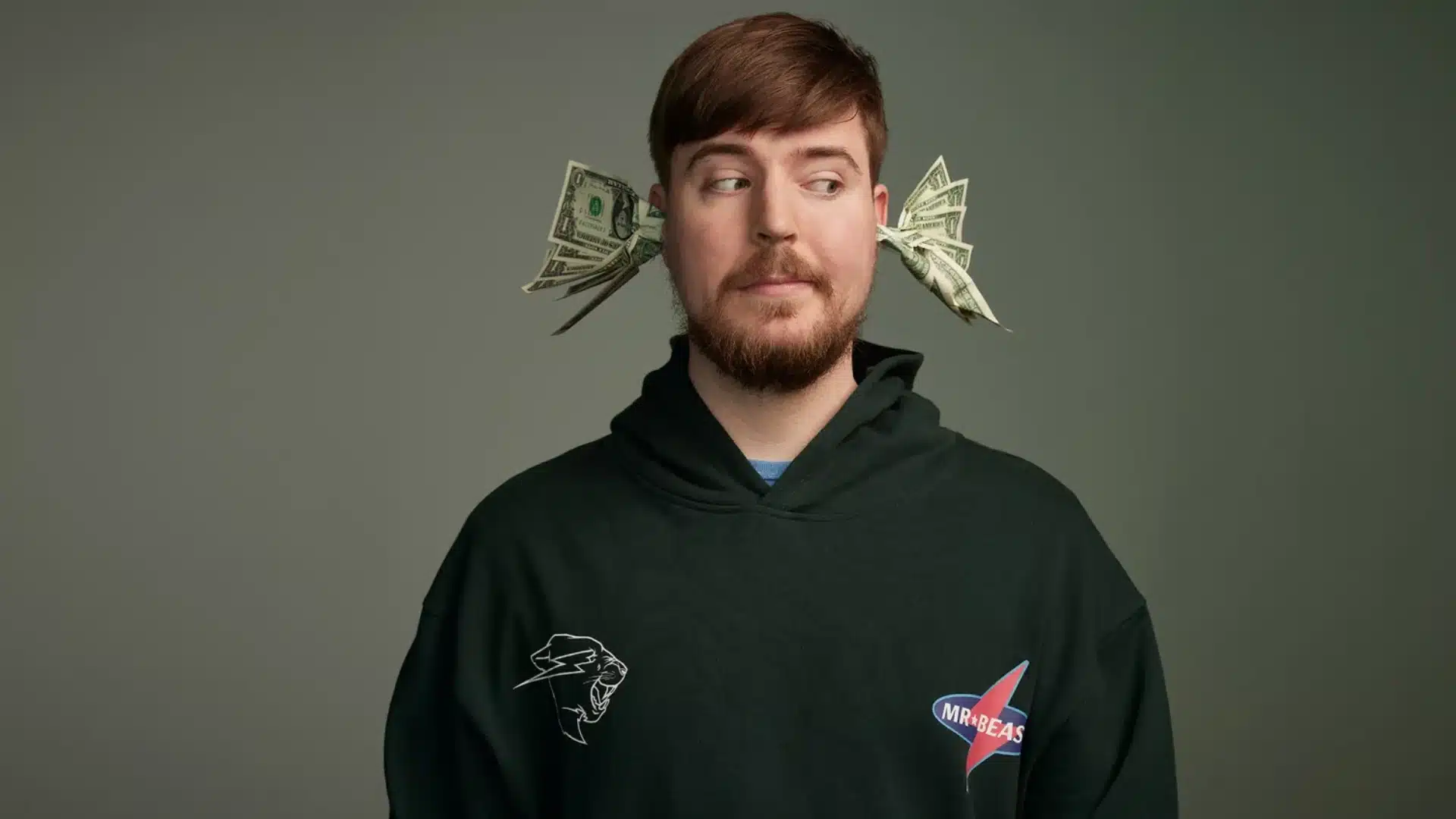 Popular YouTuber in a black hoodie posing with dollar bills tucked beside both ears