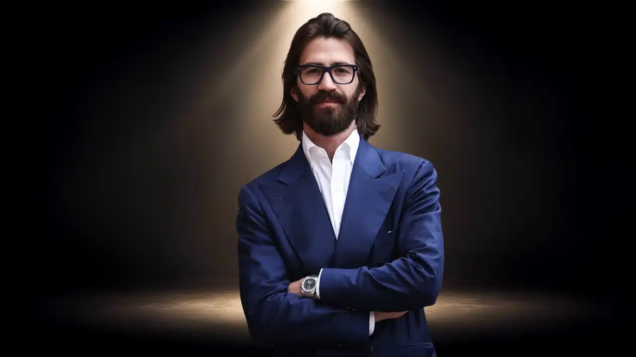 Portrait of Luca Del Vecchio with glasses and beard, wearing a blue suit with crossed arms.
