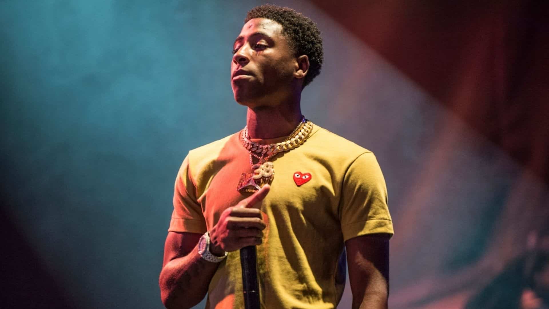 Rapper NBA YoungBoy performing on stage with a microphone under colorful lights.
