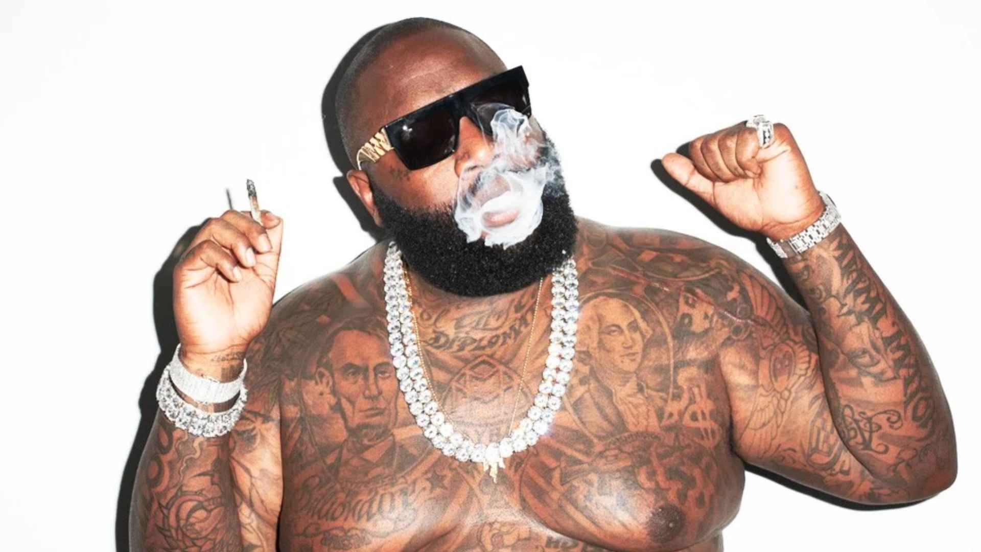 Rick Ross wearing sunglasses, jewelry, and showing tattoos while posing in a shirtless portrait.