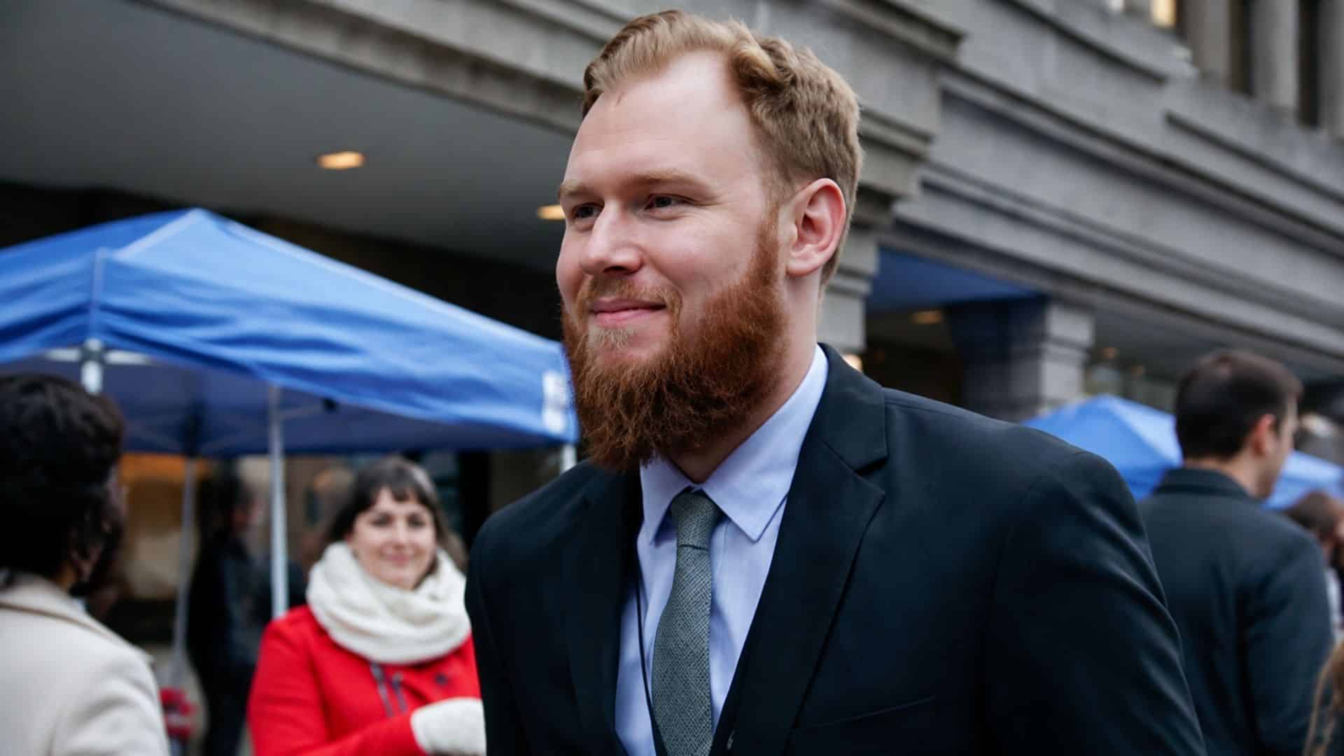 Riley Roberts wearing a suit and tie while attending an outdoor public event