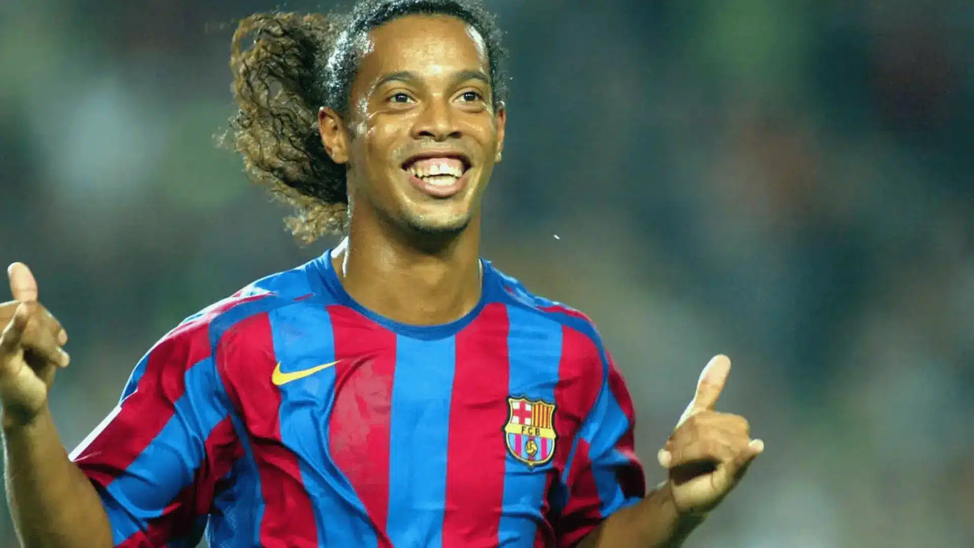 Ronaldinho smiles and celebrates while wearing Barcelona’s red and blue soccer jersey.