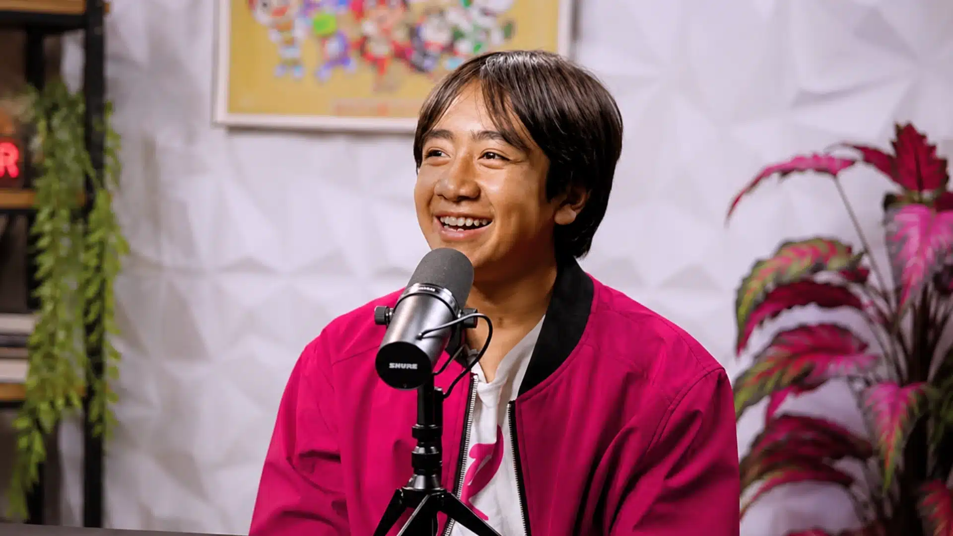 Ryan Kaji smiling into a studio microphone while wearing a bright pink jacket on set