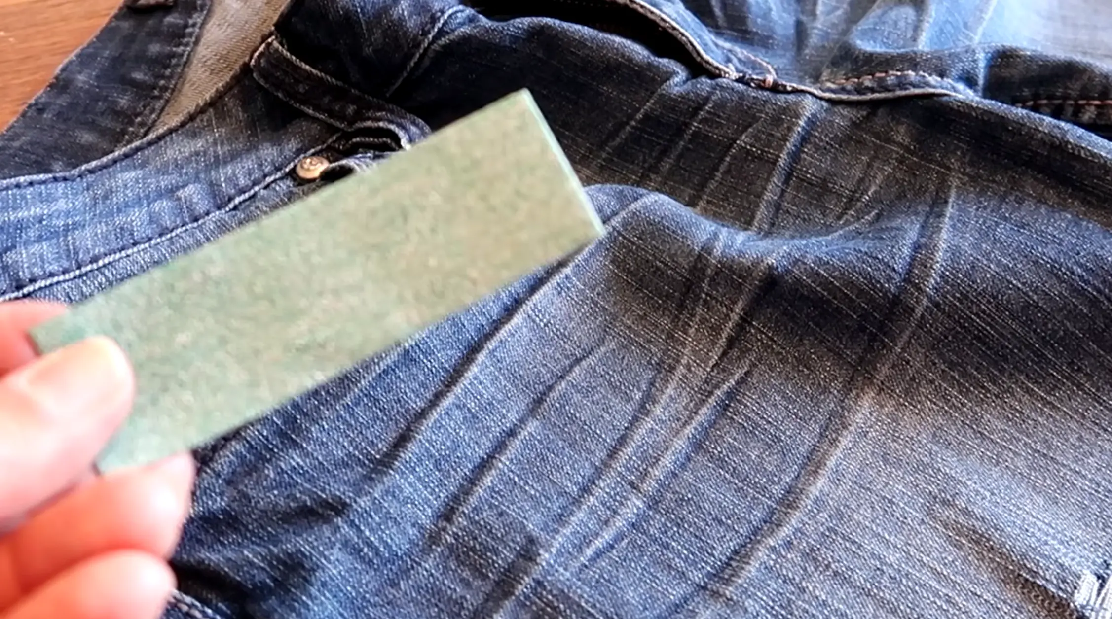 Sandpaper rubbing denim fabric to create a faded worn texture on jean