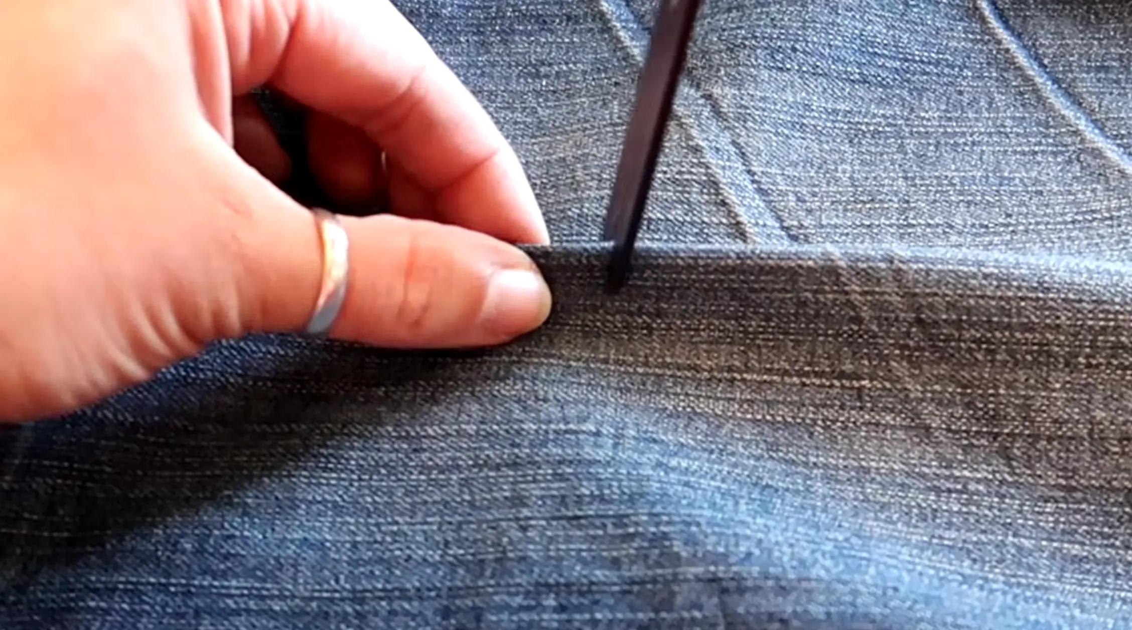 Scissors cutting a small horizontal slit into denim fabric for distressing jeans
