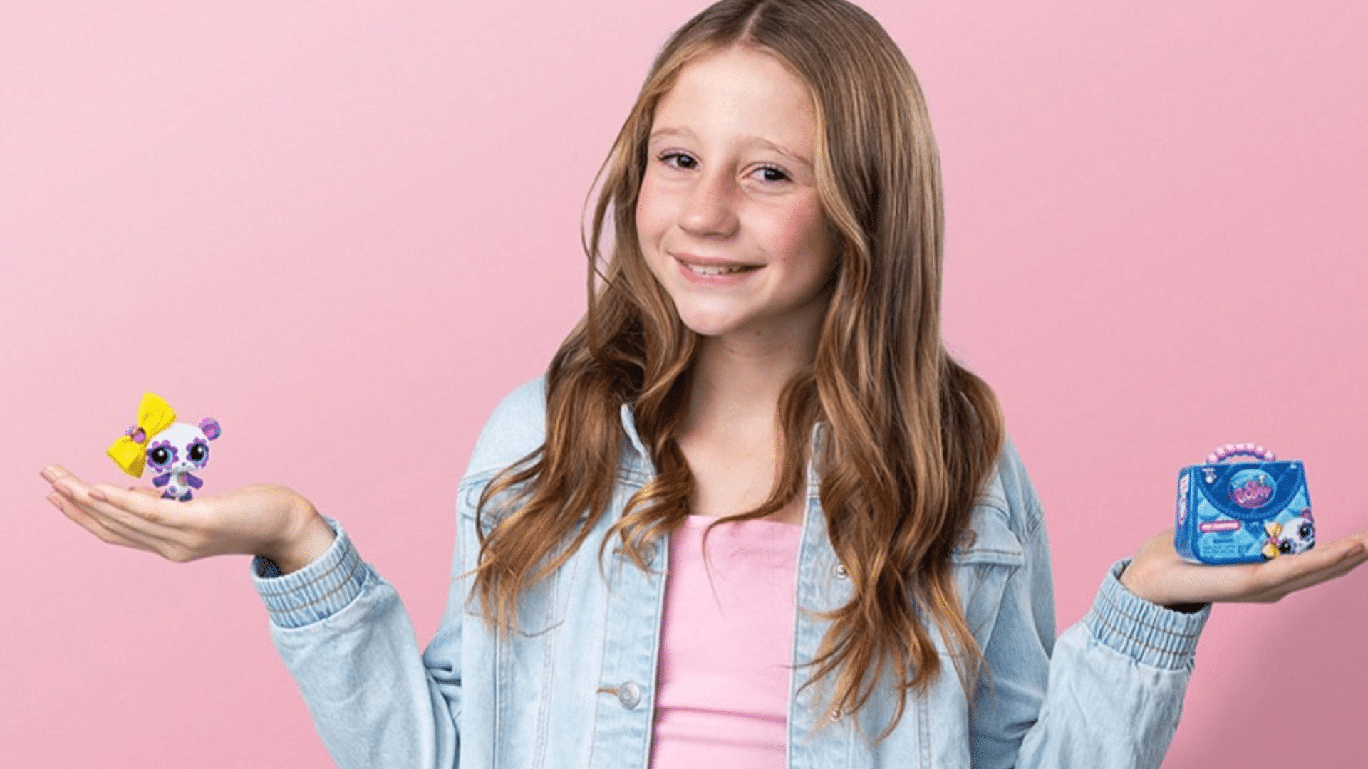 Smiling young girl holding colorful toy products against a soft pink studio background