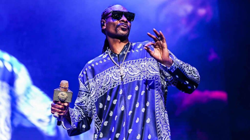 Portrait of snoop dogg with braided hair wearing a blue plaid shirt in a close up indoor setting with soft lighting