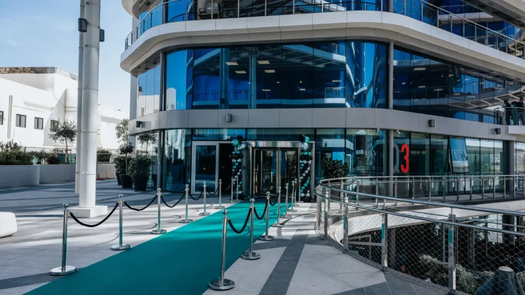 Modern building entrance with glass facade and teal carpet under sunny skies