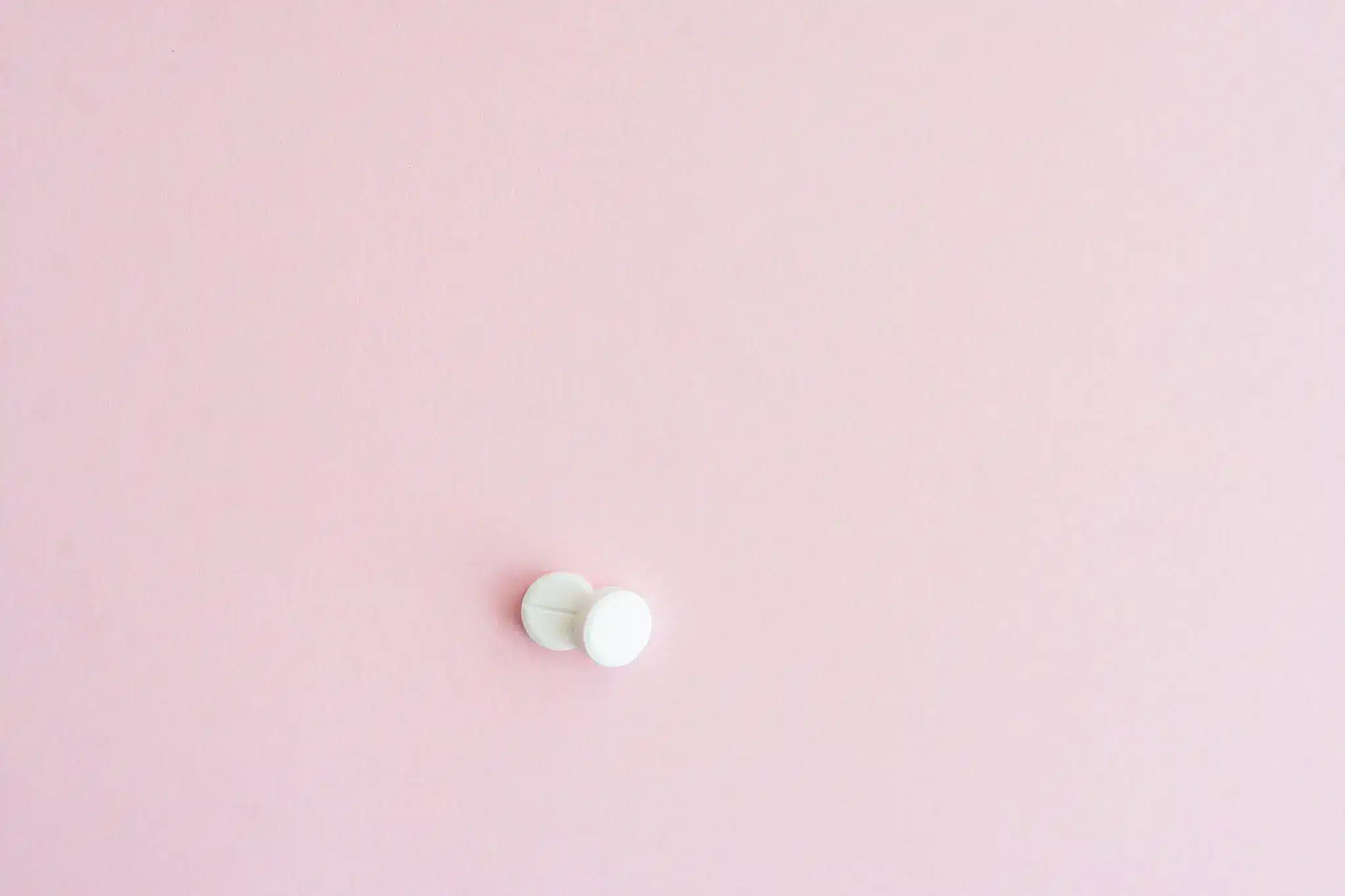 White pills on a soft pink background
